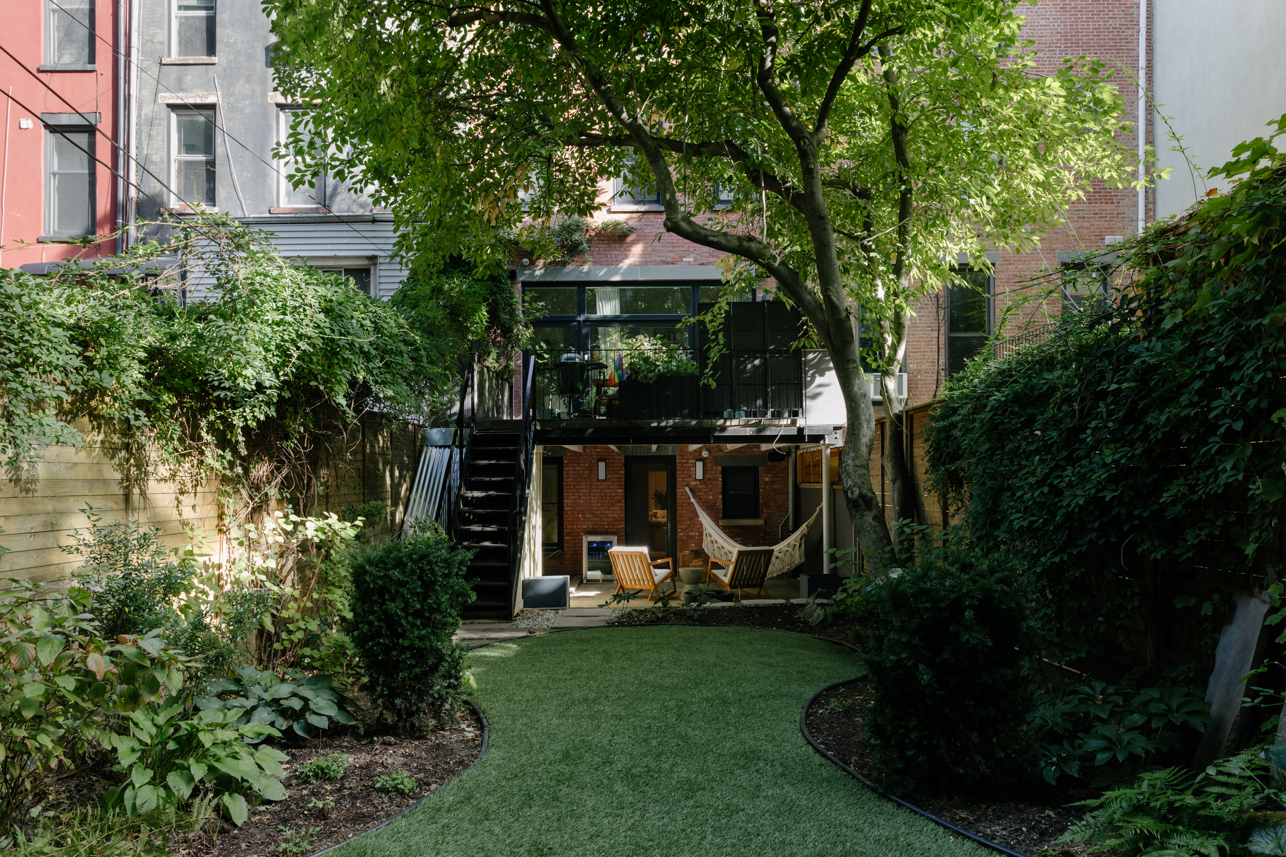 casa olympia brooklyn brownstone backyard space with lush foliage, hanging deck, and patio with hammock