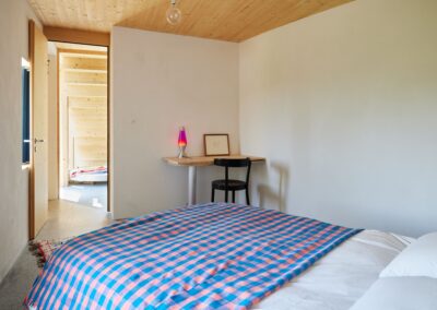 20 Casa Cometa Space Rental Interior Bedroom with bed and pink and blue checkered blanket and desk setup looking into living room